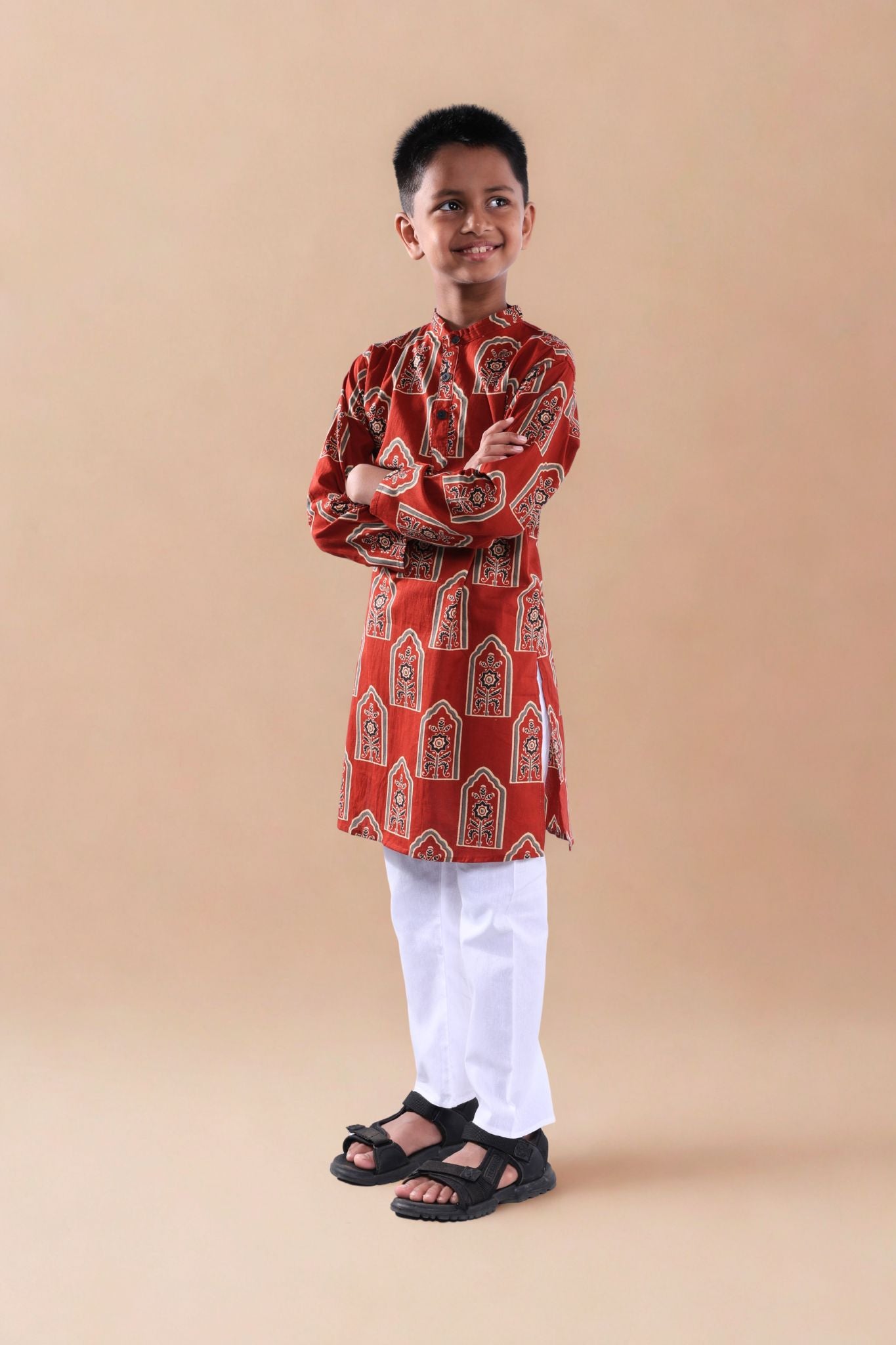 Child wearing a red patterned kurta with white pants on a beige background