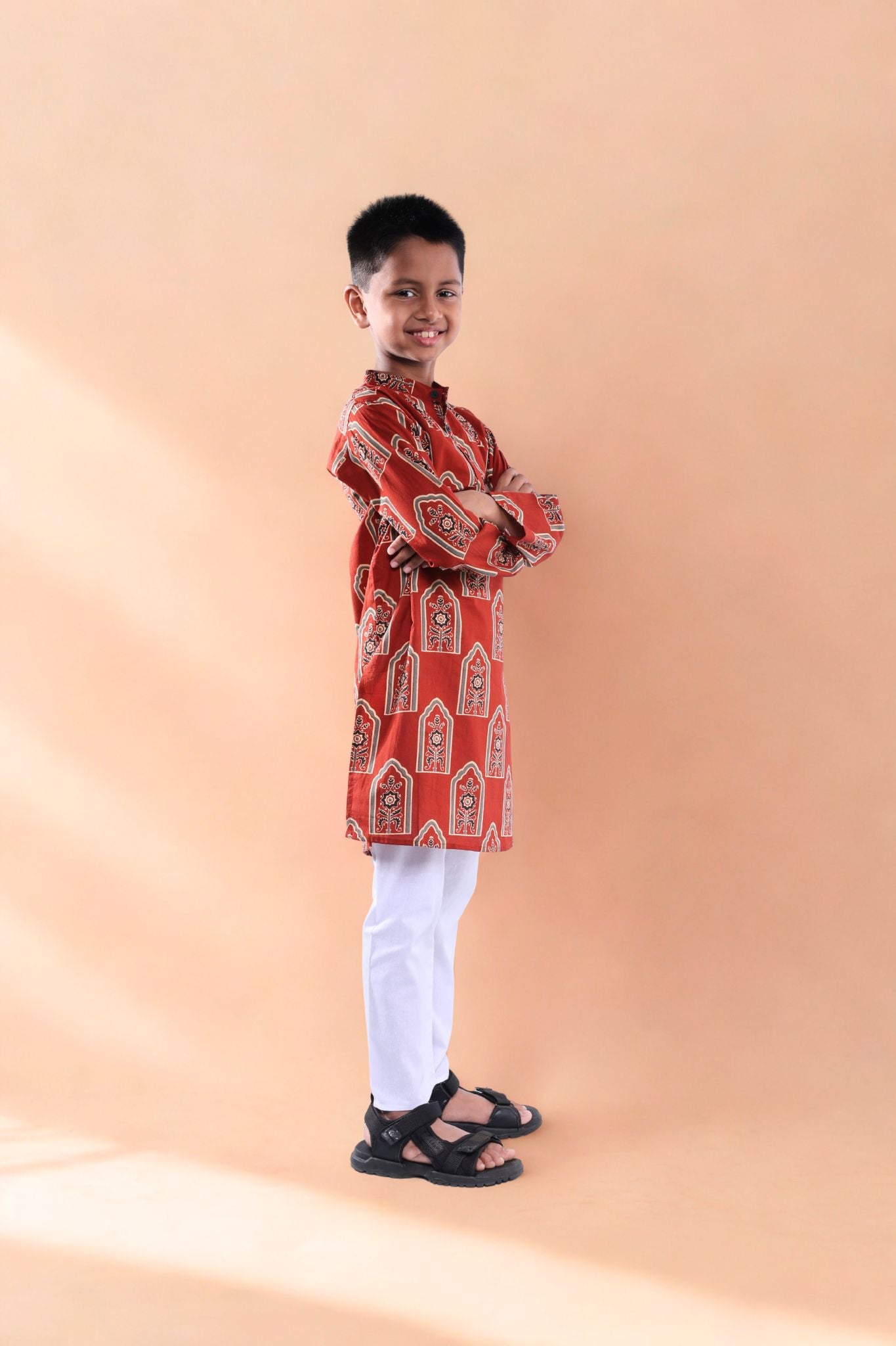 Child wearing a red traditional outfit with white pants on a beige background