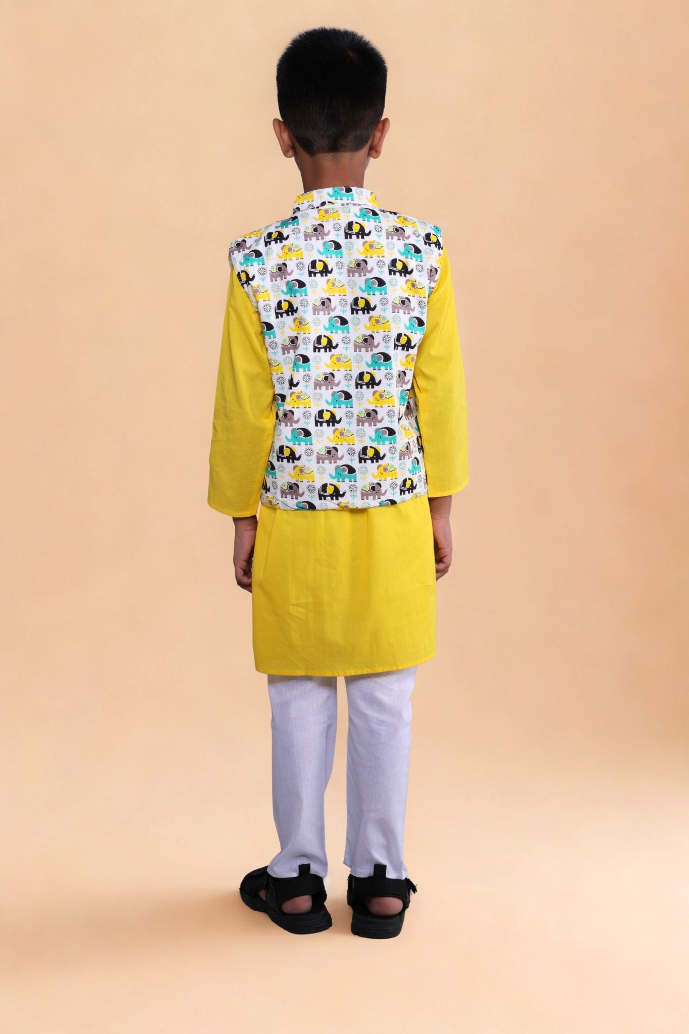Child wearing a yellow kurta with a patterned vest on a beige background